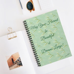 Op de afbeelding: Een groen spiraalnotitieblok met een witte achtergrond en een groen bladmotief. De tekst "May Your Harvest be Bountiful & Dreams Large!" is in groene cursieve letters op de voorkant van het notitieblok geschreven.