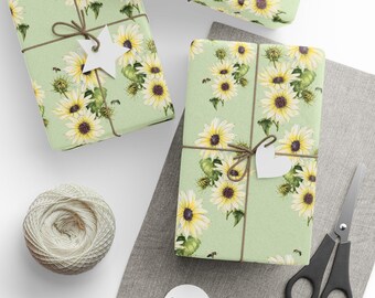 Puede incluir: Tres cajas de regalo verdes con un patrón de girasol. Las cajas están envueltas con cordel y tienen etiquetas de papel blanco adjuntas. Las cajas están sobre una superficie blanca con una superficie de tela gris en el fondo.