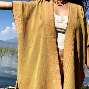 May include: A long, mustard yellow, cotton kimono with a frayed edge. The kimono is open in the front and has a striped pattern.