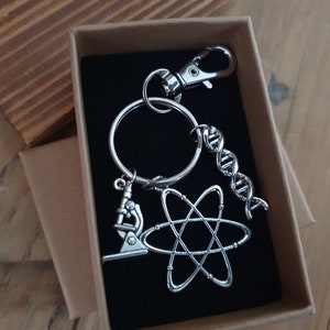 May include: A silver keyring with a microscope, atom, and DNA charm. The keyring is in a brown box with a black interior.