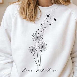 May include: White sweatshirt with a black dandelion design and butterflies flying away. The text "Your Text Here" is printed below the design.