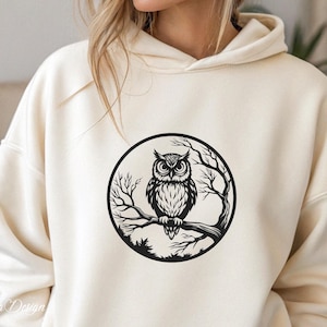 Puede incluir: Una sudadera con capucha blanca con un gr&aacute;fico en blanco y negro de un b&uacute;ho posado en una rama dentro de un c&iacute;rculo. El b&uacute;ho tiene ojos grandes y redondos y plumas detalladas.