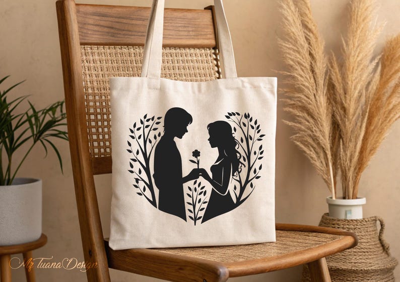 May include: A white canvas tote bag with a black silhouette of a couple holding hands in a heart shape surrounded by branches. The couple is standing in front of a tree with a flower.