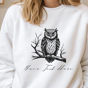 Puede incluir: Sudadera blanca con una ilustraci&oacute;n en blanco y negro de un b&uacute;ho posado en una rama. El texto "Your Text Here" est&aacute; impreso debajo del b&uacute;ho.