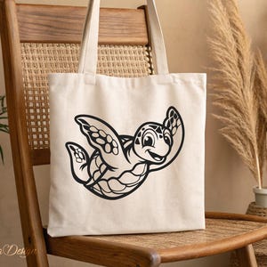 Pu&ograve; includere: Una borsa tote in tela bianca con un'illustrazione in bianco e nero di una tartaruga dei cartoni animati con un viso sorridente. La tartaruga sta nuotando con le pinne distese.