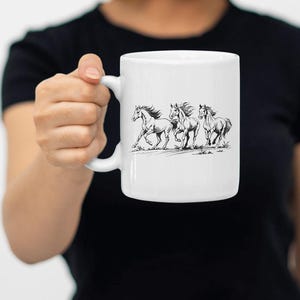 May include: White ceramic mug with a black line drawing of four horses running. The horses are in a line, with the first horse in the lead and the last horse in the back. The horses are all facing the same direction.