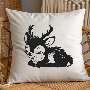 May include: A white pillow with a black silhouette of a sleeping fawn with closed eyes and antlers. The fawn is lying on its side with its head resting on its front paws.