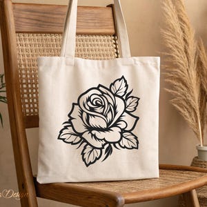 May include: A white canvas tote bag with a black silhouette of a rose printed on the front.