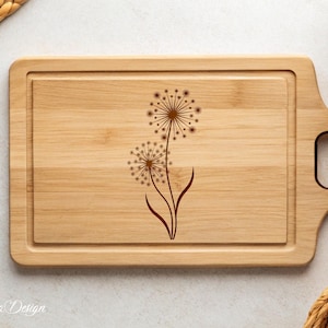 May include: A wooden cutting board with a handle, featuring a laser-engraved design of two dandelions.