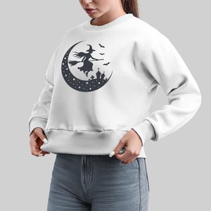 May include: White sweatshirt with a black silhouette of a witch flying on a crescent moon with stars and bats.