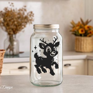 May include: A clear glass jar with a black and white silhouette of a deer with antlers. The deer is looking to the right and has a happy expression. The jar has a silver lid.