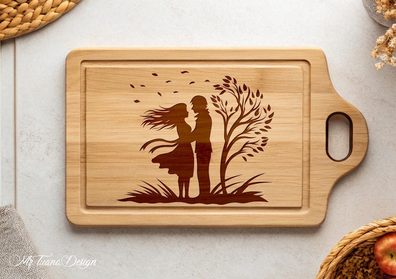 May include: A wooden cutting board with a laser-engraved design of a couple standing under a tree with leaves blowing in the wind. The design is in brown on the natural wood.