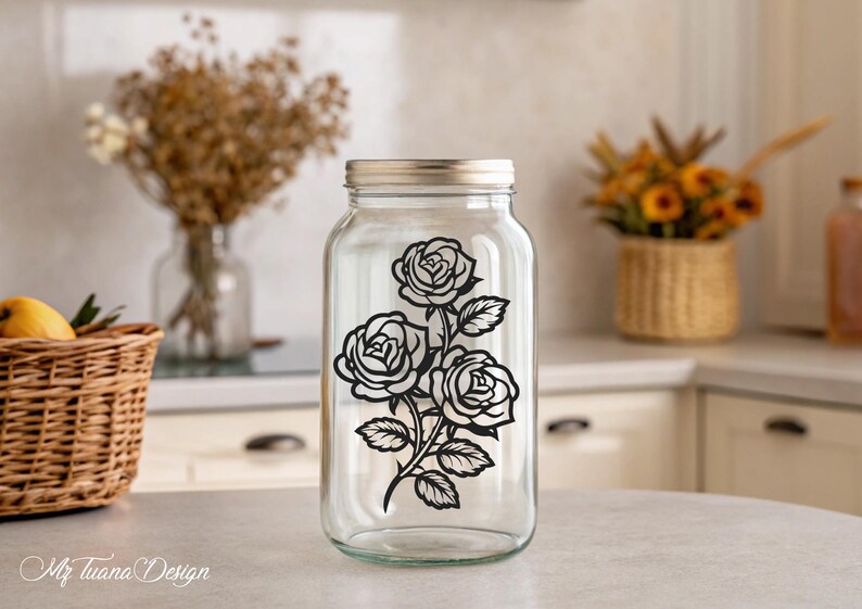 May include: A clear glass jar with a black silhouette of three roses and leaves on the front. The jar has a silver lid.