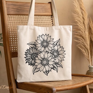 Puede incluir: Una bolsa de lona blanca con una ilustraci&oacute;n en blanco y negro de un ramo de girasoles. La bolsa tiene un asa larga y est&aacute; sentada en una silla de madera.