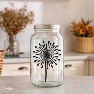 May include: A clear glass jar with a silver lid and a black dandelion silhouette decal. The jar is sitting on a white countertop.