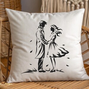 May include: A white pillow with a black silhouette of a couple holding hands. The couple is standing in a field with leaves blowing around them.