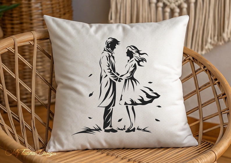 May include: A white pillow with a black silhouette of a couple holding hands. The couple is standing in a field with leaves blowing around them.
