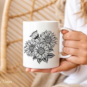 Puede incluir: Taza de cer&aacute;mica blanca con un dibujo en blanco y negro de girasoles. La taza est&aacute; siendo sostenida por la mano de una persona.