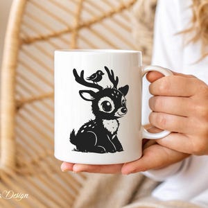 May include: White ceramic mug with a black silhouette of a deer with a bird on its head. The deer has large eyes and is sitting down.