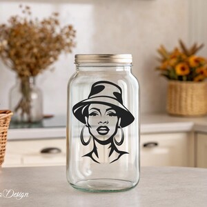 May include: A clear glass jar with a black and white silhouette of a woman wearing a hat and large earrings. The jar has a silver lid.