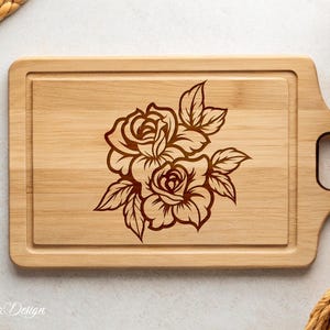 May include: A wooden cutting board with a brown floral design of roses engraved on the surface. The board has a handle on the side.