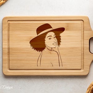 May include: A wooden cutting board with a laser-engraved design of a woman wearing a hat. The woman has curly hair and is looking to the side. The cutting board has a handle on the side.