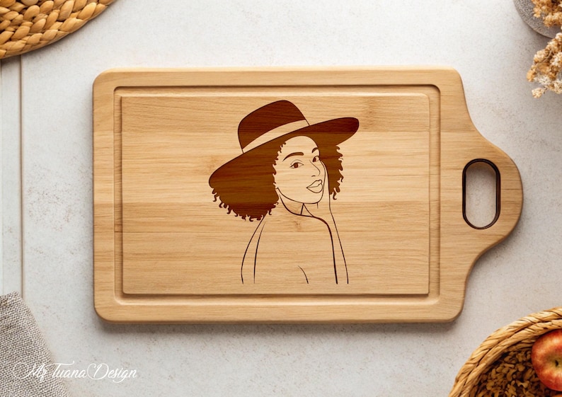 May include: A wooden cutting board with a laser-engraved design of a woman wearing a hat. The woman has curly hair and is looking to the side. The cutting board has a handle on the side.