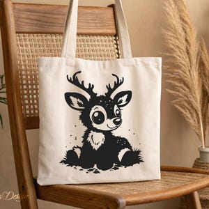 May include: A white canvas tote bag with a black and white illustration of a cartoon deer with big eyes. The deer is sitting on a white background.