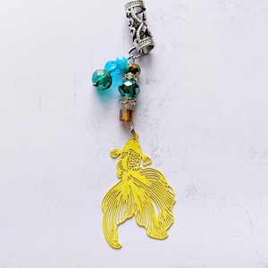 May include: A decorative charm featuring a yellow goldfish pendant. The charm includes a silver-toned tube with an openwork design, and a strand of colorful beads in shades of blue, green, and brown. The goldfish pendant has intricate cut-out details.