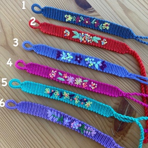 May include: Six colourful friendship bracelets with embroidered floral designs. The bracelets are numbered 1 through 6.
