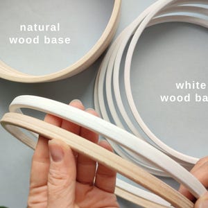 May include: Wooden embroidery hoops in natural and white finishes. The image shows several hoops, with the text "natural wood base" and "white wood base" labeling the different colors. The hoops are made of wood and are used for embroidery and other crafts.