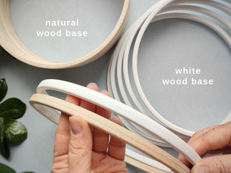 May include: Wooden embroidery hoops in natural and white finishes. The image shows several hoops, with the text "natural wood base" and "white wood base" labeling the different colors. The hoops are made of wood and are used for embroidery and other crafts.