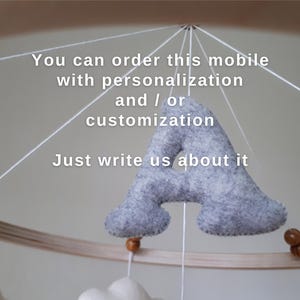 May include: A baby mobile with a wooden hoop and hanging felt shapes. A large gray felt letter "A" is suspended in the center. The text on the image says, "You can order this mobile with personalization and/or customization. Just write us about it."