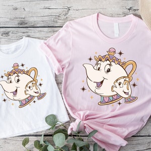 May include: Two t-shirts featuring a cartoon image of Mrs. Potts and Chip from Disney's Beauty and the Beast. The larger shirt is pink and the smaller shirt is white.