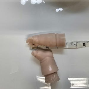 Pu&ograve; includere: Due braccia di bambola in vinile liscio di colore chiaro con dita definite e pieghe sui polsi. Un metro a nastro bianco &egrave; posizionato contro il braccio superiore, mostrando una lunghezza di circa 8,9 cm dalla punta delle dita al bordo.