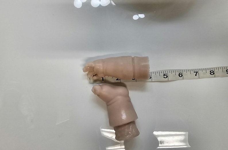 Pu&ograve; includere: Due braccia di bambola in vinile liscio di colore chiaro con dita definite e pieghe sui polsi. Un metro a nastro bianco &egrave; posizionato contro il braccio superiore, mostrando una lunghezza di circa 8,9 cm dalla punta delle dita al bordo.