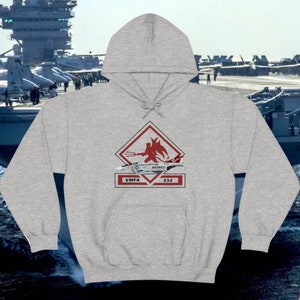 May include: A light gray hoodie featuring a graphic of a red devil with a trident, a jet, and the text "VMFA 232 MARINES". The background shows an aircraft carrier and fighter jets.