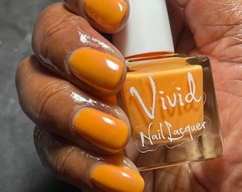 May include: A hand holding a bottle of orange nail polish. The bottle is labeled "Vivid Nail Lacquer".