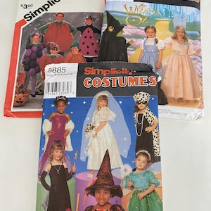 May include: Several Simplicity costume pattern envelopes are displayed, featuring various Halloween and dress-up designs. The patterns showcase costumes like a witch, a princess, and characters from "The Wizard of Oz". The envelopes are colorful and feature images of the finished costumes.