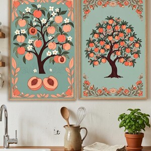May include: Two framed art prints featuring peach trees. The trees are depicted with peach-colored fruit, white blossoms, and green leaves against a teal background. The frames are a light brown color, and the artwork has a vintage, botanical style.