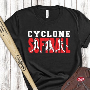 Può includere: Maglietta nera con testo bianco che recita "CYCLONE SOFTBALL" con silhouette bianche di giocatrici di softball nelle lettere. Nell'immagine sono presenti anche una mazza da baseball in legno, una palla da baseball e un guanto da baseball in pelle marrone.