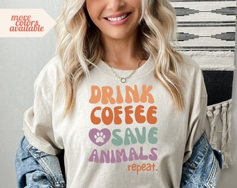 Könnte beinhalten: Ein hellbeiges T-Shirt mit dem Text "Drink Coffee Save Animals Repeat." in einer Retro-Schriftart mit einem Pfotenabdruck in einem Herzen.