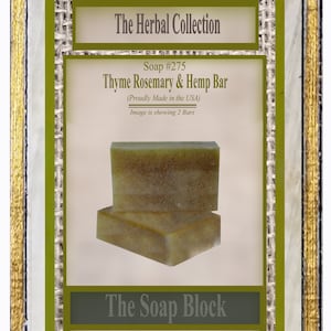 Könnte beinhalten: Zwei Stück Seife mit Thymian, Rosmarin und Hanf, hergestellt in den USA. Die Seife ist hellgrün und hat eine raue Textur. Die Seife ist in einer grün-goldenen Schachtel verpackt mit dem Text "The Herbal Collection" und "The Soap Block".