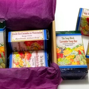 May include: A gift box filled with four bars of handmade soap. The soaps are wrapped in colorful paper with images of fruits and vegetables. The soaps are labeled with the names "The Soap Block Lavender Soap Bar", "Green Tea Cucumber & Watermelon Handmade Artisan Soap", "The Soap Block Lavender Soap Bar", and "The Soap Block Tropical Soap Bar".