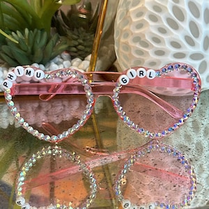 May include: Pink heart-shaped sunglasses with rhinestones and the words "Phi Mu Girl" spelled out in white letters.