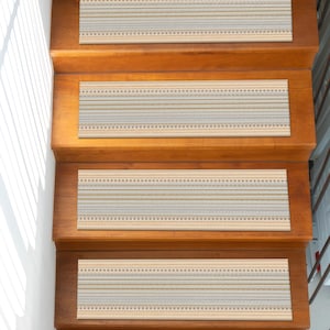 Könnte beinhalten: Treppenstufen mit einem beige-, blau- und goldfarbenen Streifenmuster sind auf Holztreppen installiert. Die Trittflächen haben ein strukturiertes Aussehen und sind rechteckig. Die Treppe besteht aus hellbraunem Holz und befindet sich in einem Haus.