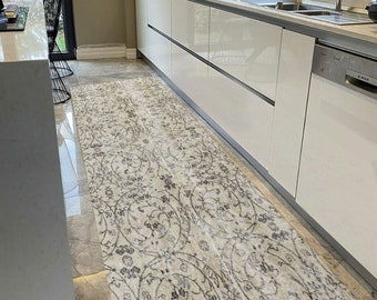 May include: A white and gray patterned runner rug with a floral design. The rug is placed in a modern kitchen with white cabinets and a stainless steel dishwasher.