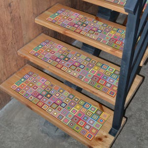 May include: Wooden staircase with colorful, geometric patterned stair treads. The treads feature a repeating square design in various colors, including red, blue, green, and yellow. A black metal railing is visible on the right side of the stairs.