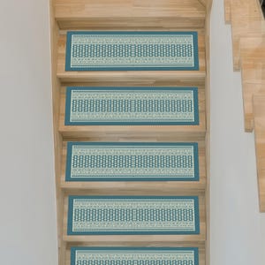 May include: Stair treads with a teal border and a repeating geometric pattern in cream and teal. The treads are rectangular and placed on wooden stairs, providing a decorative and functional element for home decor.