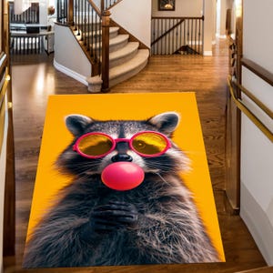 May include: A rectangular rug featuring a raccoon with sunglasses and a pink bubble gum bubble against a bright yellow background. The raccoon is gray and black with pink-framed sunglasses. The rug is placed on a wooden floor.